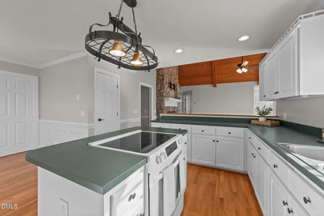 a kitchen that has a sink a microwave oven a stove and white cabinets with wooden floor
