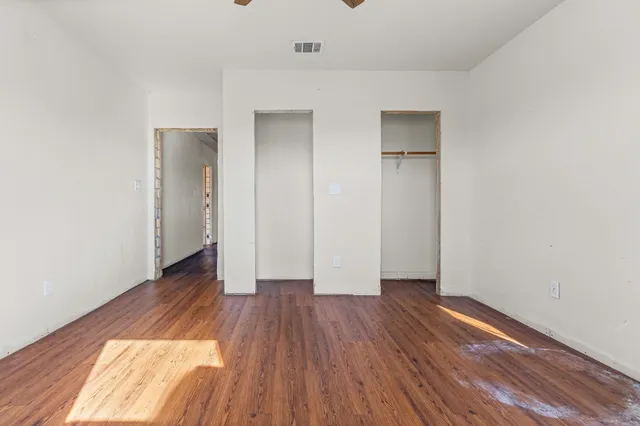 an empty room with wooden floor chandelier fan and windows