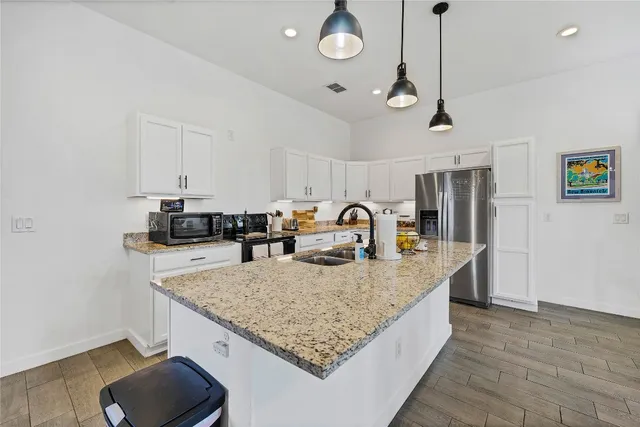 a kitchen with stainless steel appliances granite countertop a sink dishwasher and a refrigerator with wooden floor