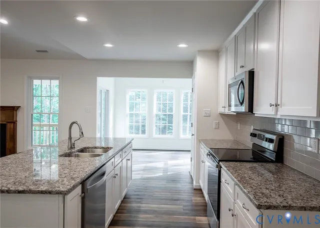 a kitchen with granite countertop kitchen island stainless steel appliances a sink stove and cabinets