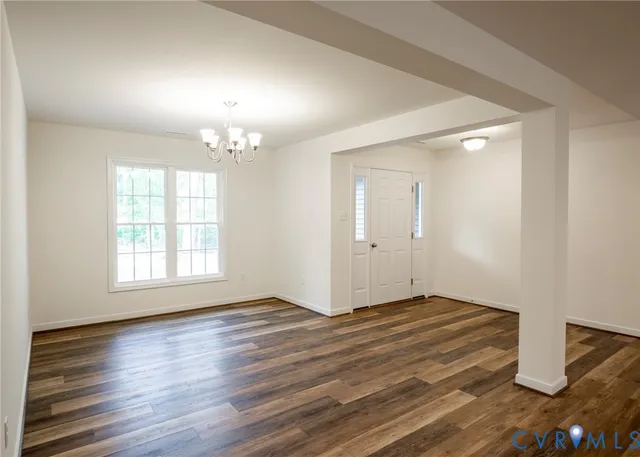 an empty room with wooden floor chandelier and windows