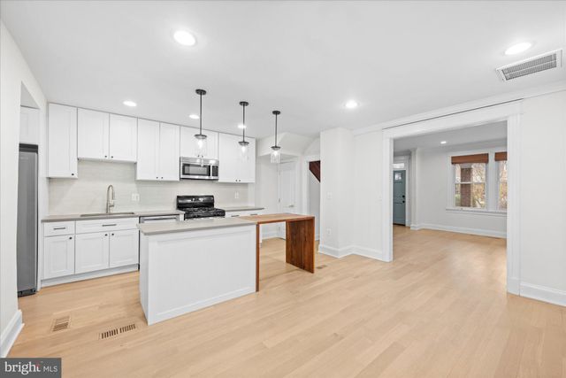 a kitchen with granite countertop a sink stove a refrigerator and white cabinets with wooden floor