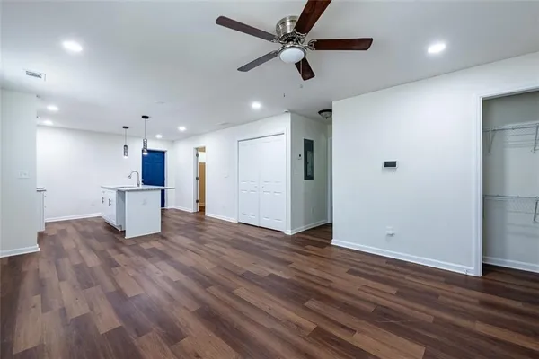 an empty room with wooden floor a ceiling fan and kitchen view