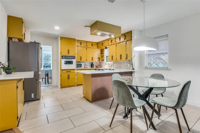 a dining hall with stainless steel appliances kitchen island granite countertop a table chairs and a refrigerator