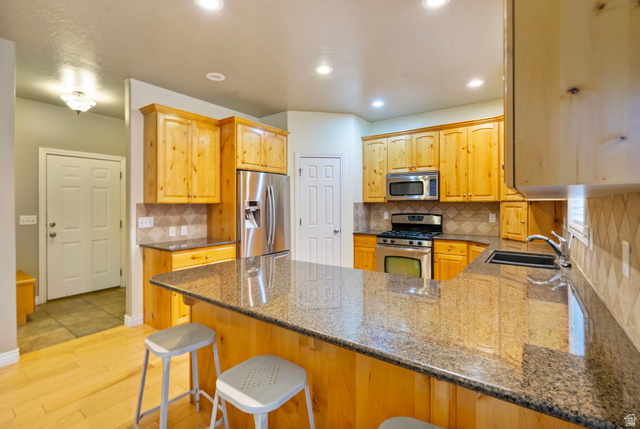 557 South 1470th Street East Springville, UT 84663 - Photo 12 of 46 Kitchen featuring dark stone counters, stainless steel appliances, a peninsula, light hardwood floors, and tasteful backsplash