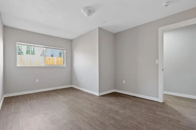 a view of an empty room with wooden floor and a window