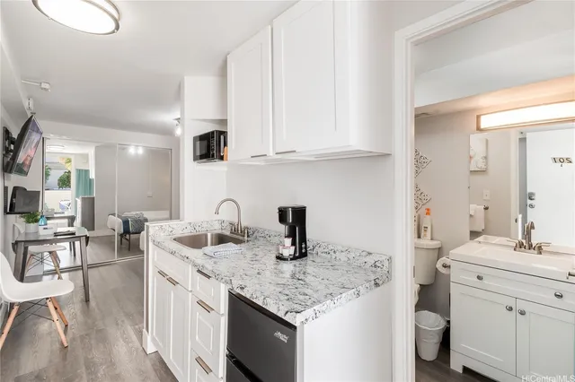 a kitchen with granite countertop a sink dishwasher a stove and white cabinets with wooden floor