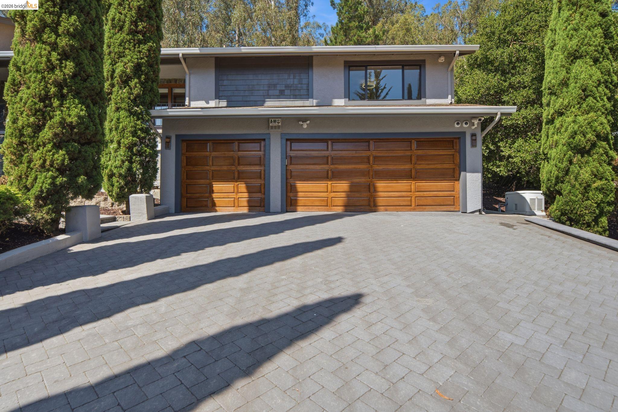 11133 Golf Links Road Oakland, CA 94605 - Photo 4 of 57 Contemporary exterior with a two-car garage featuring wood-paneled doors, a paver driveway, and mature vertical landscaping