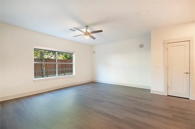 an empty room with wooden floor chandelier fan and windows