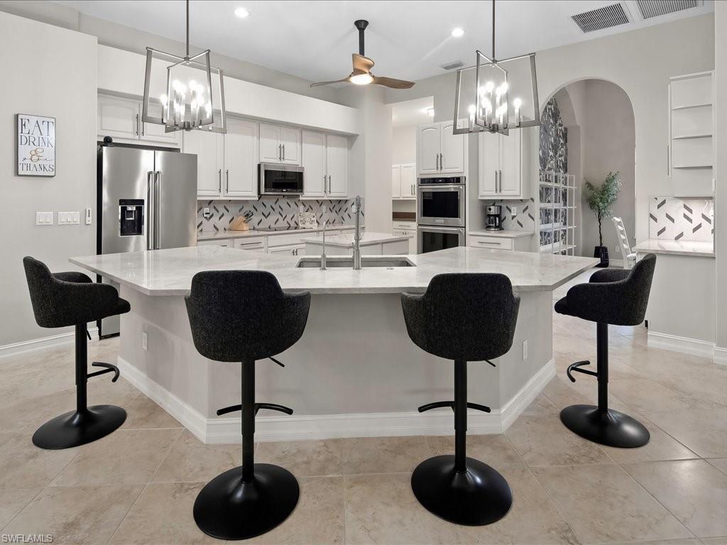 2360 19th Street Southwest Naples, FL 34117 - Photo 17 of 50 Kitchen featuring appliances with stainless steel finishes, a sink, arched walkways, white cabinetry, and decorative backsplash
