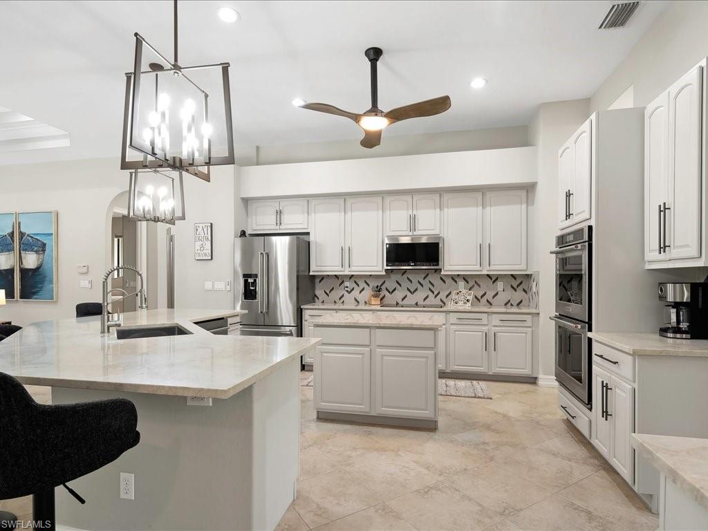 2360 19th Street Southwest Naples, FL 34117 - Photo 19 of 50 Kitchen featuring a large island with sink, appliances with stainless steel finishes, a sink, backsplash, and a ceiling fan