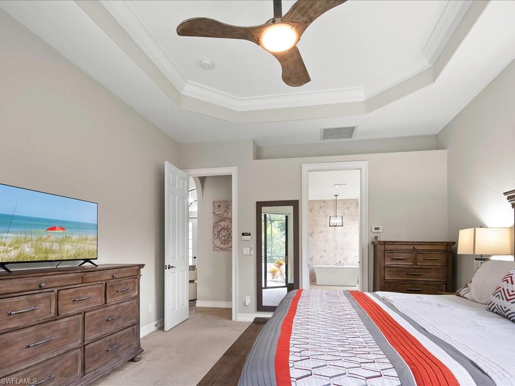 2360 19th Street Southwest Naples, FL 34117 - Photo 29 of 50 Bedroom featuring a tray ceiling, crown molding, ensuite bathroom, light colored carpet, and a ceiling fan