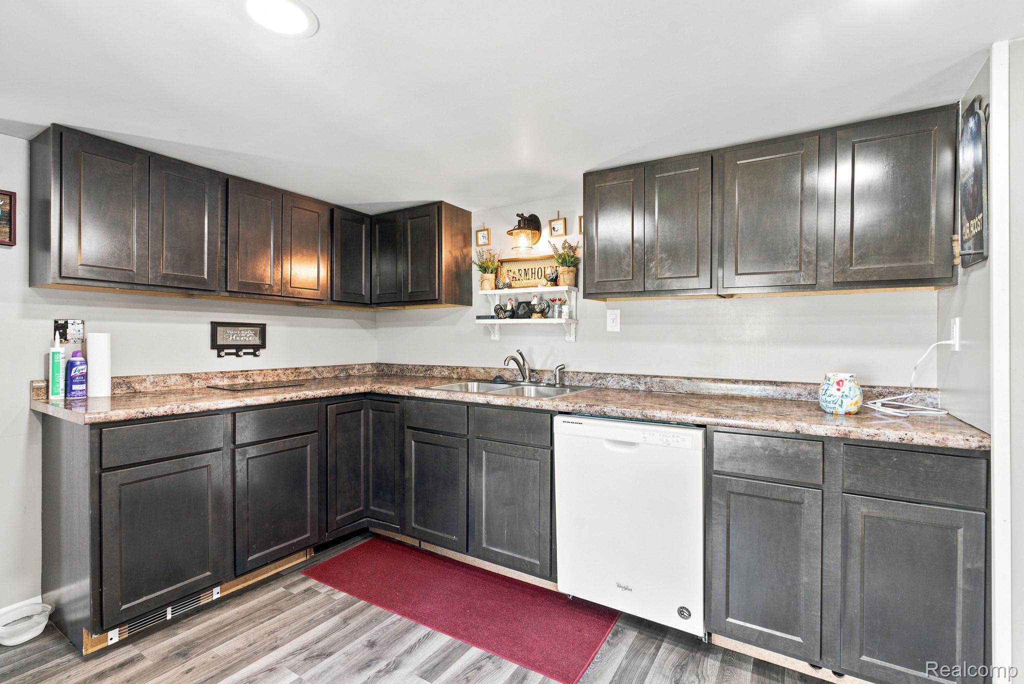 4201 Galbraith Line Road Croswell, MI 48422 - Photo 11 of 39 Corner kitchen featuring dark wood-finish cabinetry, speckled countertops, a double basin stainless steel sink, and a white built-in dishwasher