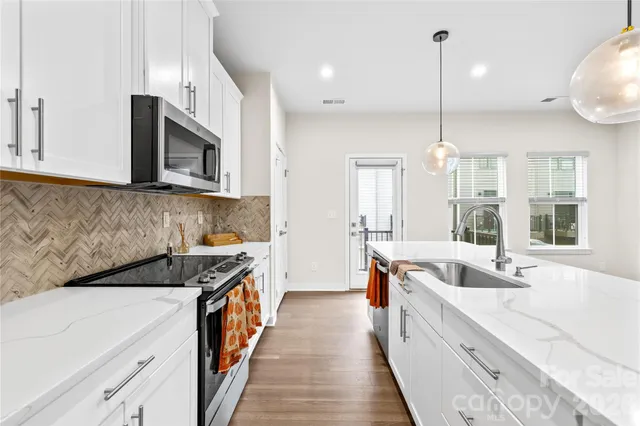 a kitchen with stainless steel appliances kitchen island granite countertop a refrigerator a stove oven and white cabinets with wooden floor