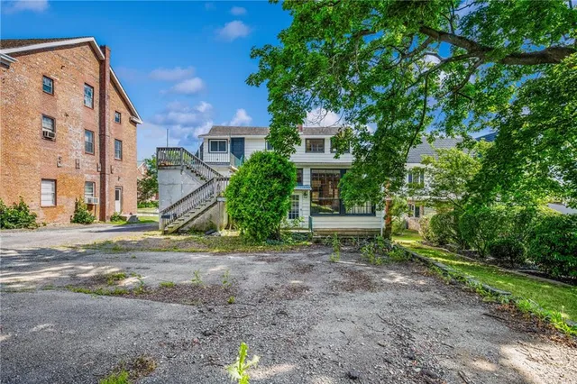a view of a white house next to a yard with potted plants