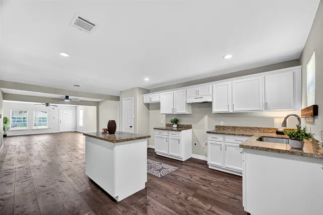 a large kitchen with stainless steel appliances granite countertop a stove top oven a sink a refrigerator and white cabinets with wooden floor