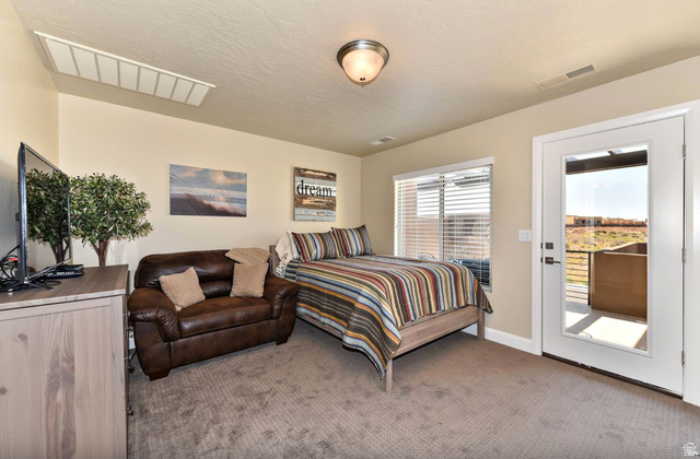 1622 Canyon Tree Drive St. George, UT 84770 - Photo 22 of 34 Carpeted room featuring a ceiling-mounted light fixture, a window with horizontal blinds, and a glass-paneled door opening to an outdoor patio with metal railings and a desert landscape beyond