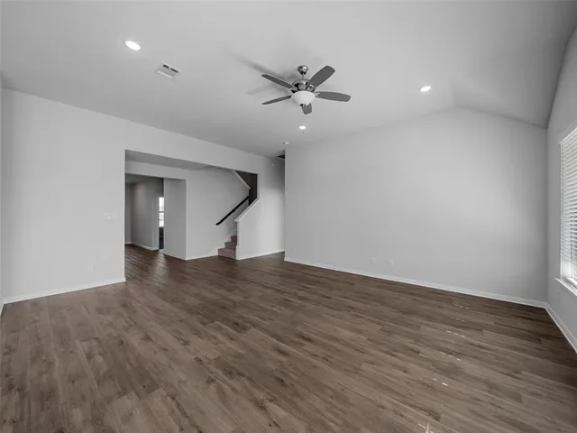 a view of an empty room with wooden floor and a ceiling fan