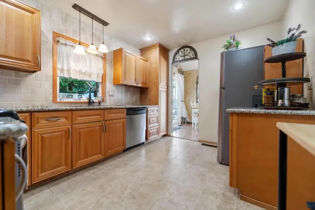 a kitchen with granite countertop a refrigerator a sink a stove and wooden cabinets