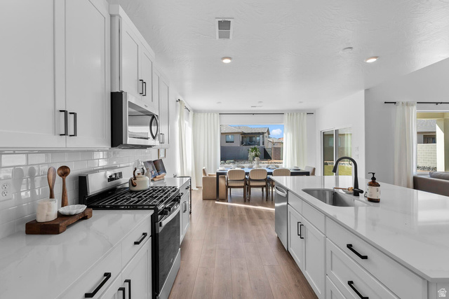 382 North Rhyolite Drive, Unit 111 Hurricane, UT 84737 - Photo 36 of 37 Open-concept kitchen featuring white shaker cabinetry, stainless steel appliances, a subway tile backsplash, and light wood-finish flooring
