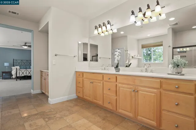 a spacious en suite bathroom with a granite countertop sink a large mirror and a chandelier