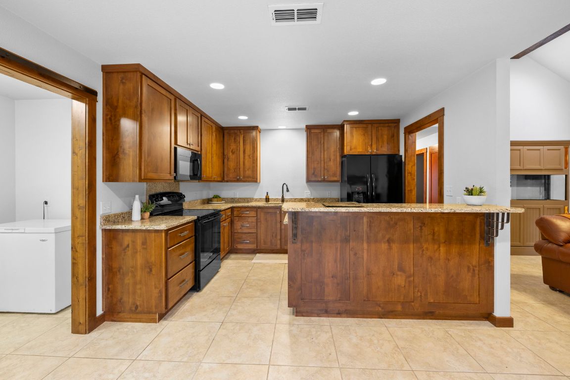 315 Flying R Ranch Road Spring Branch, TX 78070 - Photo 27 of 39 Kitchen with light stone counters, black appliances, brown cabinets, and recessed lighting