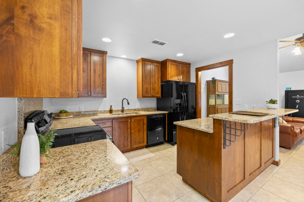 315 Flying R Ranch Road Spring Branch, TX 78070 - Photo 28 of 39 Kitchen featuring light stone counters, brown cabinets, black appliances, recessed lighting, and light tile patterned floors