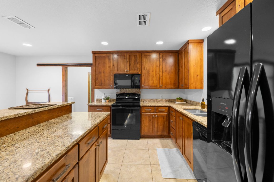 315 Flying R Ranch Road Spring Branch, TX 78070 - Photo 29 of 39 Kitchen featuring black appliances, light stone counters, brown cabinetry, recessed lighting, and light tile patterned floors