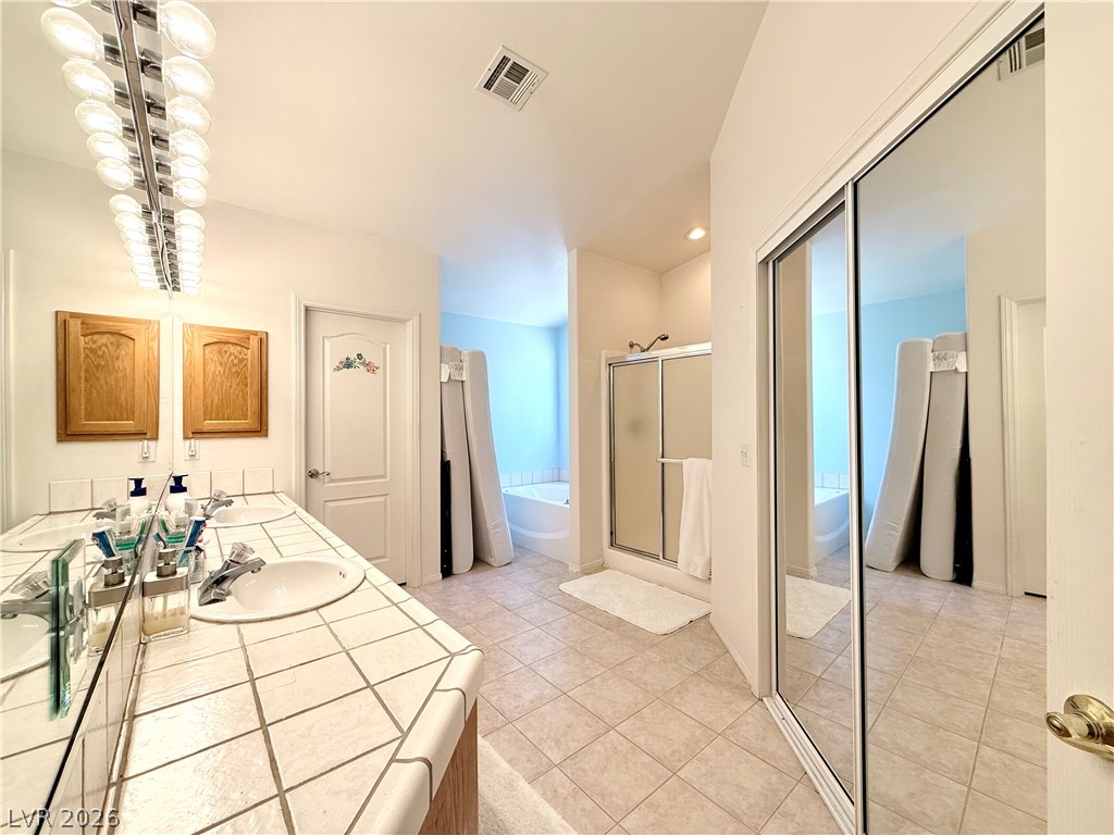 1220 East Gamebird Road Pahrump, NV 89048 - Photo 15 of 49 Owner's suite with double vanities and tiled countertops create a spacious and functional primary bathroom retreat.