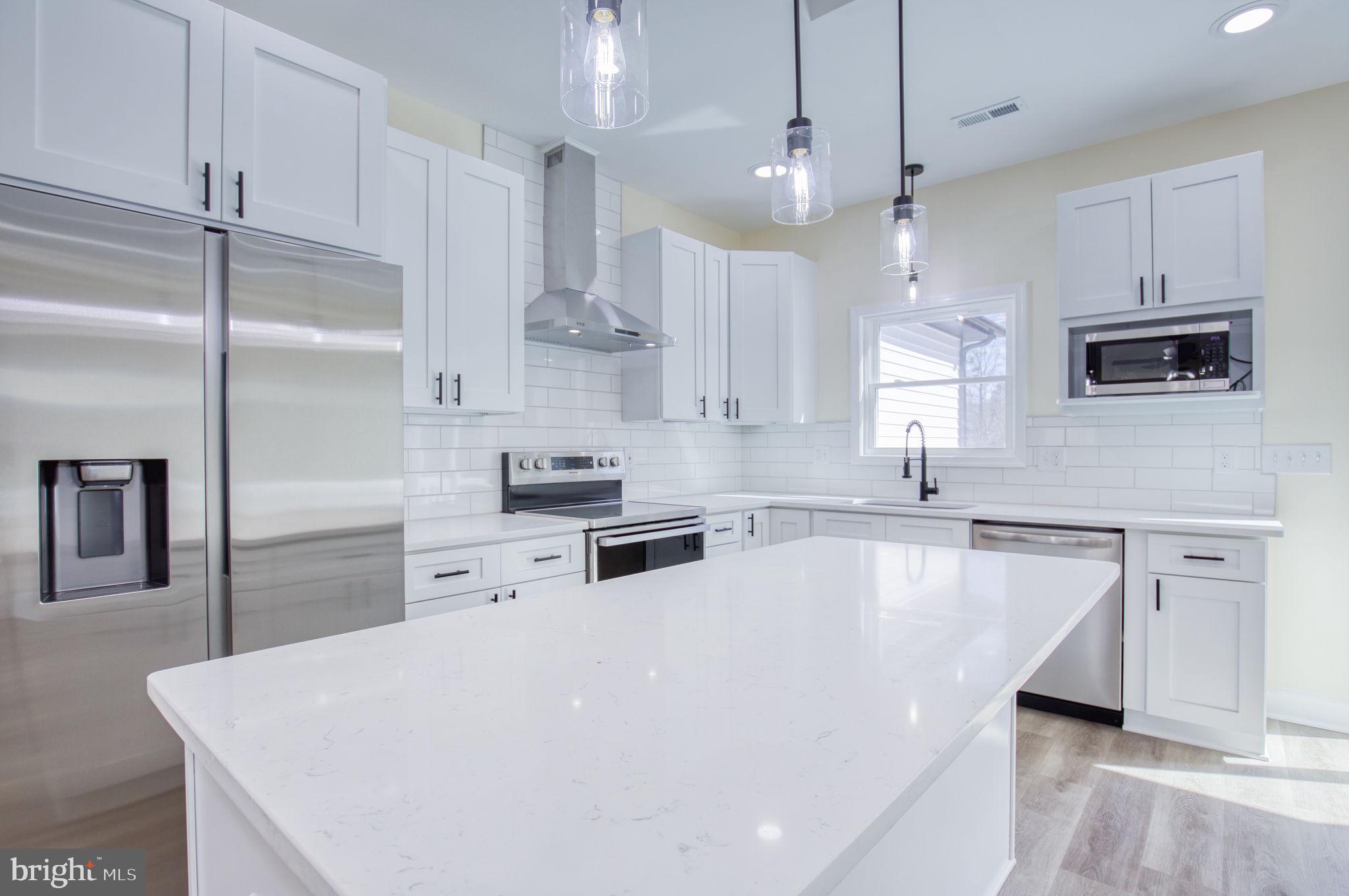 49 Poplar Lane Colonial Beach, VA 22443 - Photo 2 of 42 a large white kitchen with kitchen island a sink a stove a refrigerator and chairs