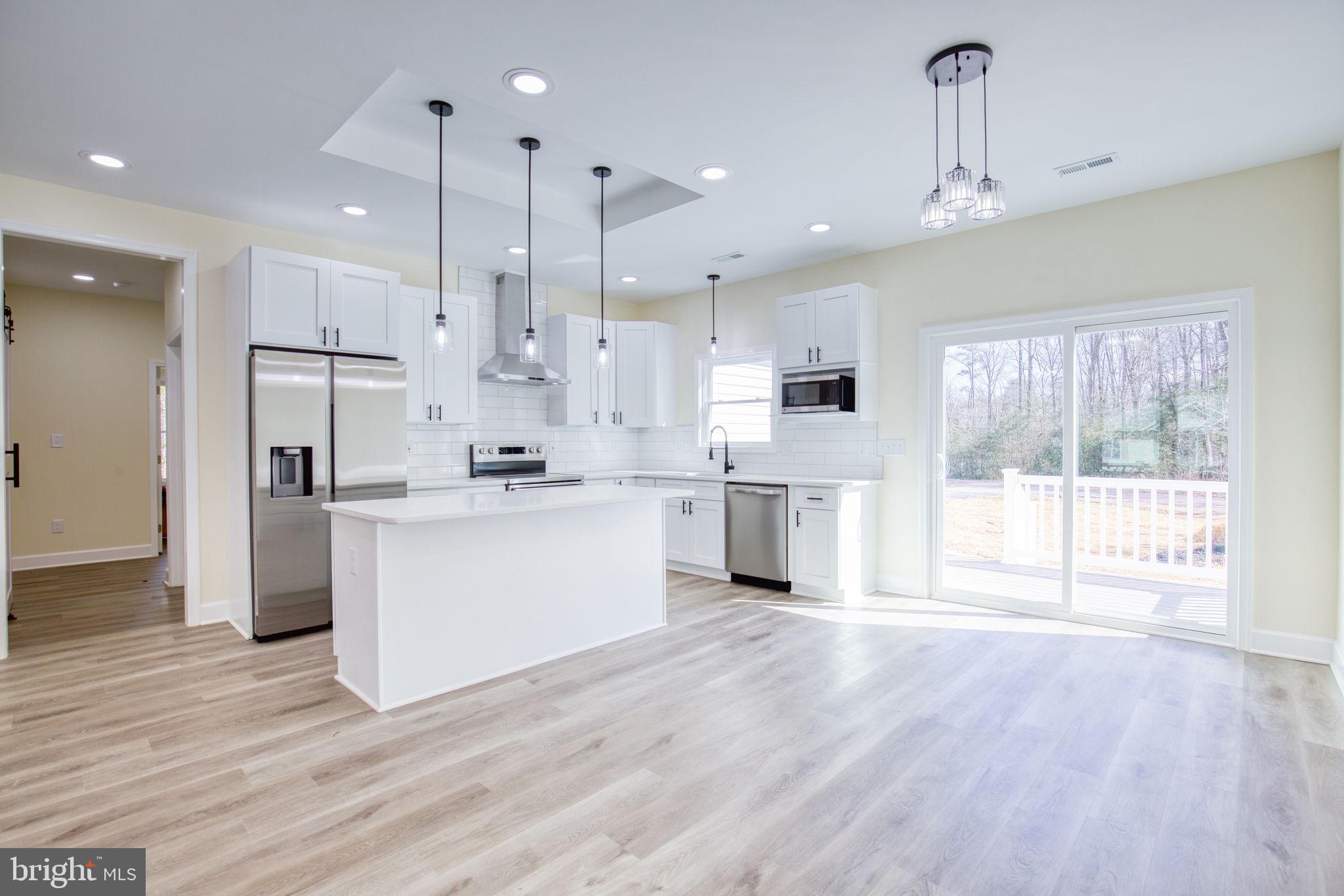 49 Poplar Lane Colonial Beach, VA 22443 - Photo 4 of 42 a large kitchen with stainless steel appliances kitchen island granite countertop a stove a sink a refrigerator white cabinets and wooden floor next to a window