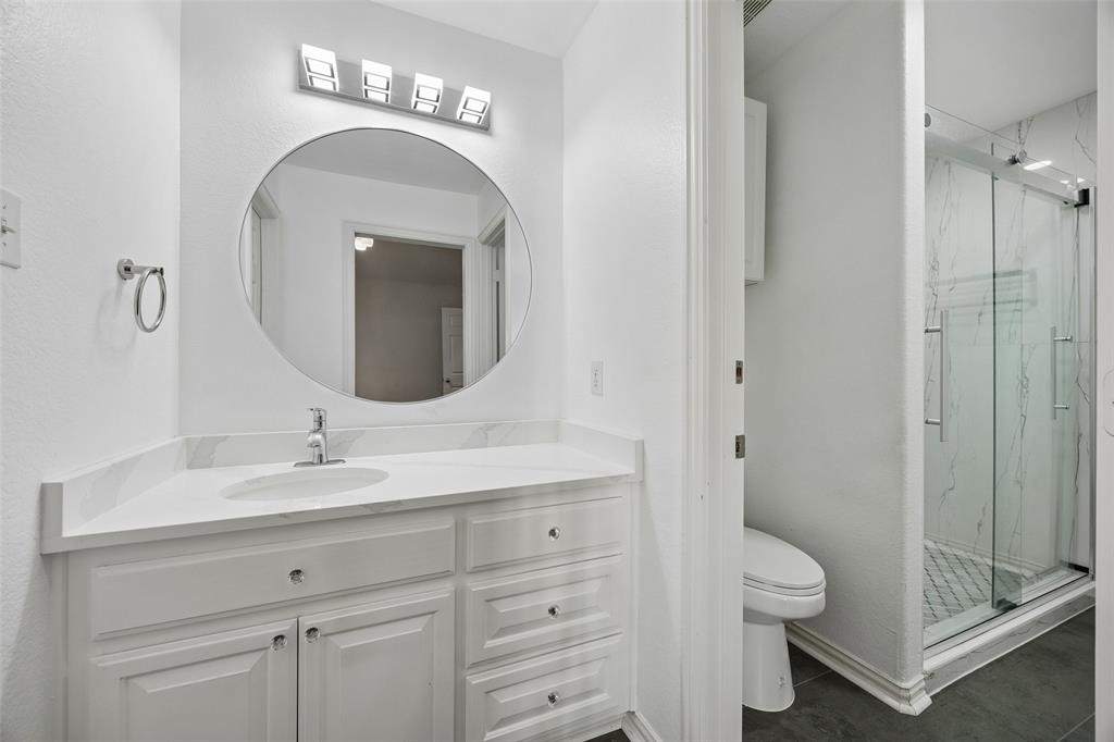 2865 Ridge View Road Frisco, TX 75034 - Photo 29 of 38 White vanity with integrated sink and chrome faucet, large circular mirror, four-light vanity fixture, glass-enclosed shower with subway tile, and dark floor tiling