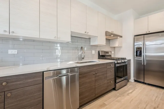 a kitchen with stainless steel appliances granite countertop a sink a stove a refrigerator and white cabinets