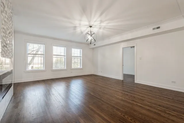 an empty room with wooden floor chandelier fan and windows