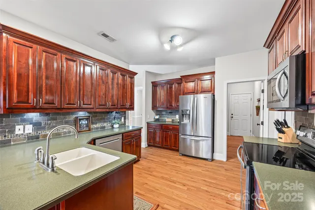 a kitchen with stainless steel appliances granite countertop a refrigerator a sink dishwasher a stove and white countertops with wooden floor