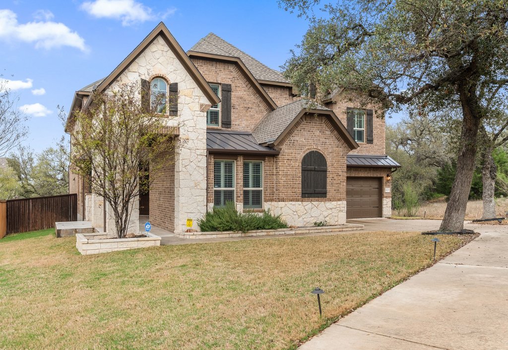 French country inspired facade featuring a standing seam roof, stone siding, brick siding, driveway, and an attached garage