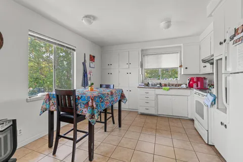 a kitchen that has white cabinets a stove and a dining table with chairs