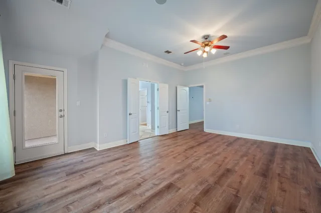 a view of an empty room with wooden floor and a ceiling fan