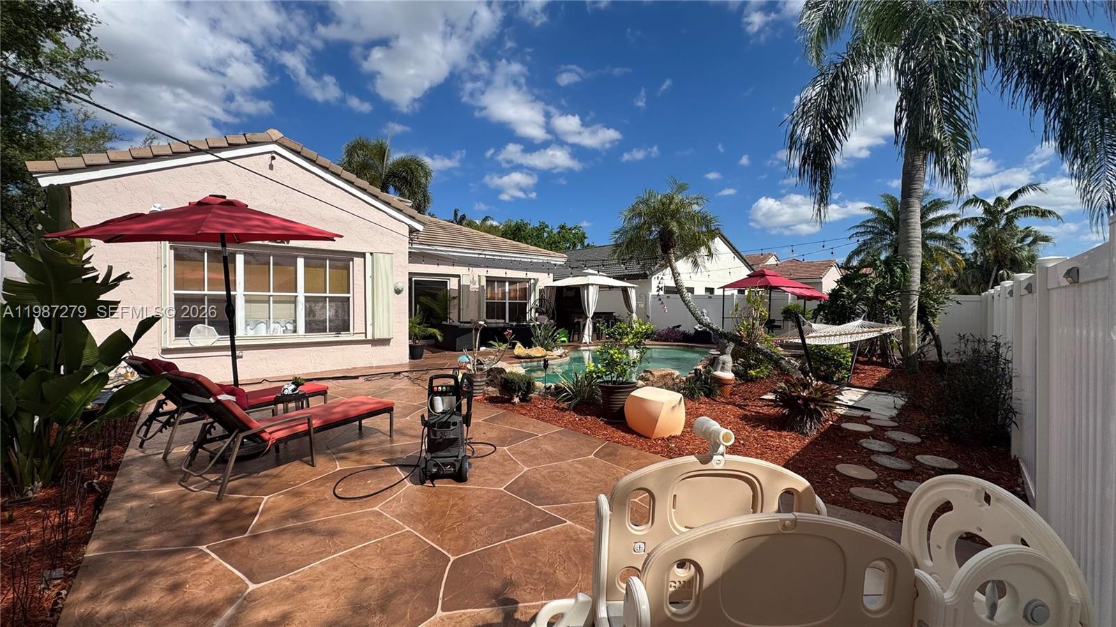 4220 Southwest 153rd Avenue Miramar, FL 33027 - Photo 32 of 34 a view of a patio with table and chairs under an umbrella with palm trees