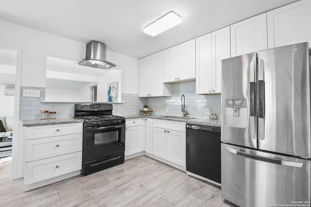 a kitchen with granite countertop a refrigerator stove and white cabinets
