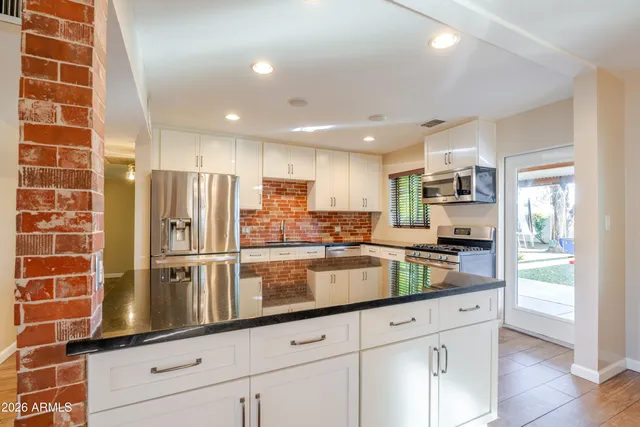 a kitchen with stainless steel appliances granite countertop a refrigerator a stove a sink and white cabinets with wooden floor