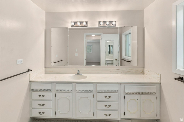 15295 North 5400th Street West Riverside, UT 84334 - Photo 27 of 54 White vanity with multiple storage drawers and cabinet doors, an integrated sink, a light-toned countertop, and a wall-mounted tri-fold mirror