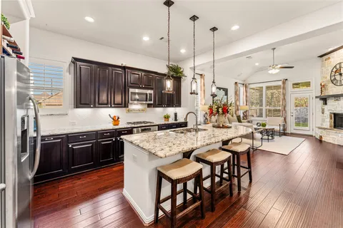 a kitchen with stainless steel appliances granite countertop a stove top oven a sink dishwasher a dining table and chairs with wooden floor