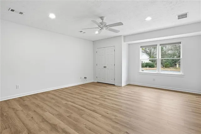 an empty room with wooden floor ceiling fan and windows