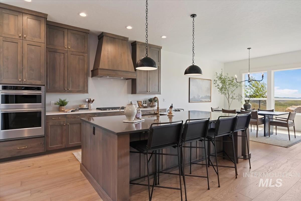 7615 Brown Way Eagle, ID 83714 - Photo 13 of 43 Open-concept kitchen featuring custom wood cabinetry, stainless steel double ovens, a large kitchen island with seating, and light wood-finish flooring