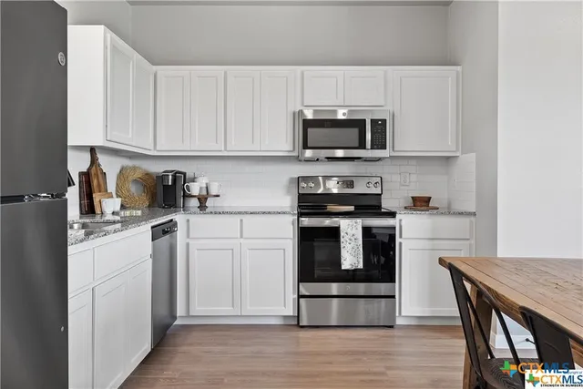 a kitchen with stainless steel appliances granite countertop a stove top oven a sink dishwasher and white cabinets with wooden floor