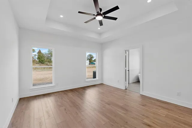 an empty room with wooden floor chandelier fan and windows