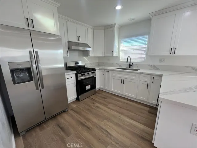 a kitchen with stainless steel appliances granite countertop a refrigerator a sink a stove and white cabinets