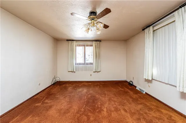 an empty room with chandelier fan and windows