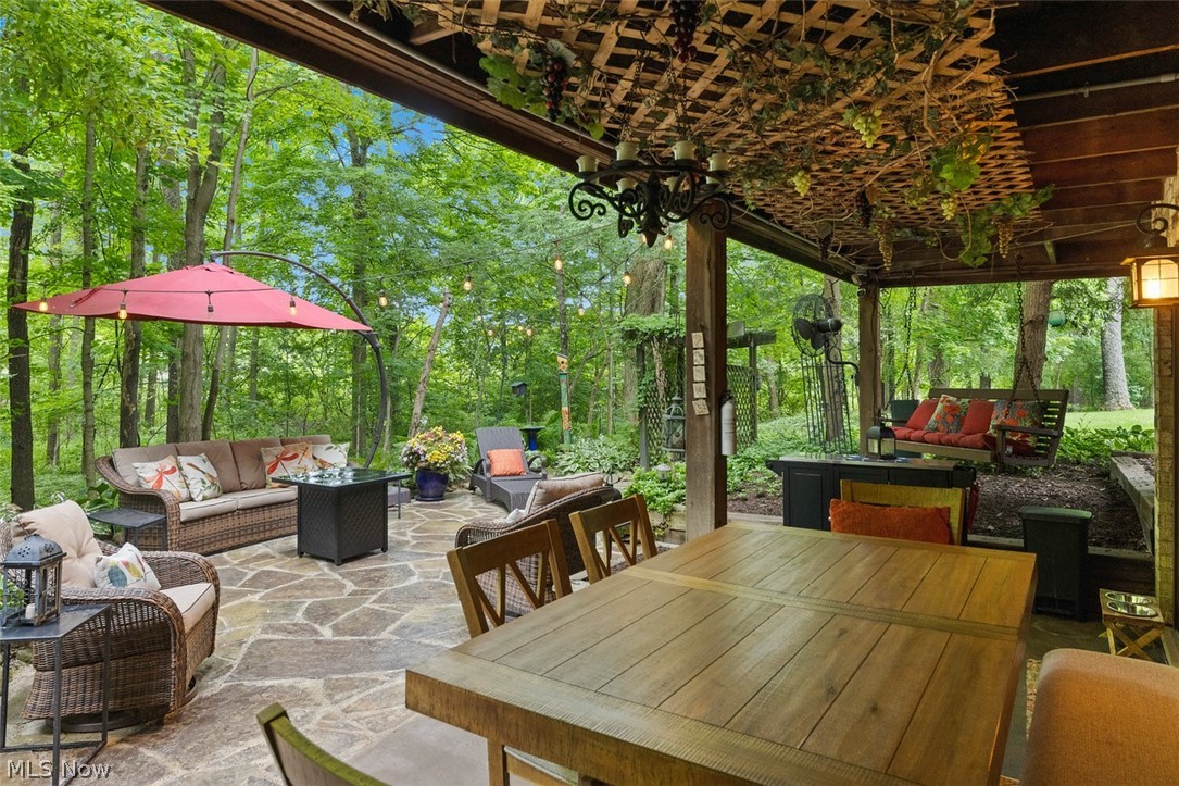 171 Granger Road, Unit 107 Medina, OH 44256 - Photo 36 of 41 Covered outdoor patio featuring extensive flagstone flooring, a wooden trellis ceiling, built-in wall lighting, a large wooden dining table, and a ceiling-mounted chandelier. A wooden trellis over the walkway (Stays).